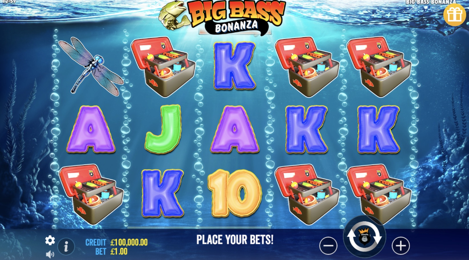 Pantalla del juego Big Bass Bonanza con gráficos vibrantes. El fondo submarino muestra plantas marinas y burbujas. Los rodillos tienen símbolos coloridos como una libélula, cajas de pesca y letras brillantes (A, K, J, 10). El título del juego aparece en la parte superior en colores brillantes. La interfaz incluye iconos claros para el crédito y la apuesta, que complementan el atractivo diseño visual.